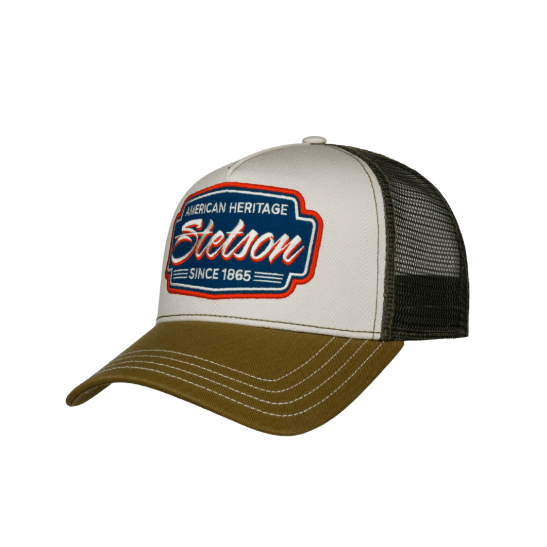 A trucker-style baseball cap with a white front panel, black mesh back, and olive brown brim. The front panel features a prominent embroidered logo that reads 'American Heritage Stetson Since 1865' in red, white, and blue.